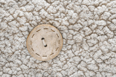 Beige button sewn on white wool background closeup
