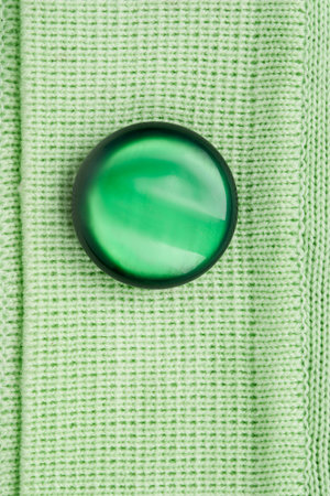 Large green button sewn on green knit cardigan closeup