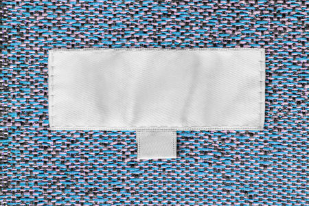 Blank white clothes label stitched on colorful tapestry fabric background