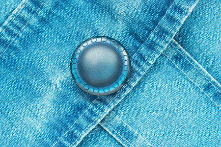 Blue plastic clothes button on blue denim fabric