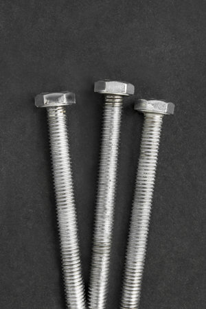 Three long steel bolt screws on black studio background