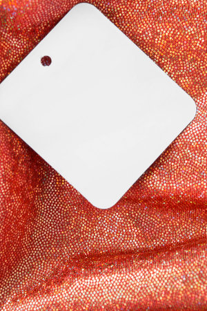 Blank paper clothes label on red metallic fabric closeup