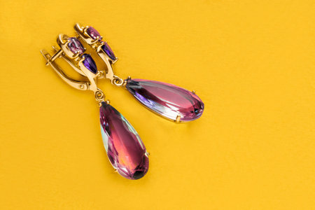 Elegant pink crystal golden earrings on yellow studio backgroundの写真素材