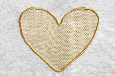 Golden heart embroidered on gray cotton fabric as a background