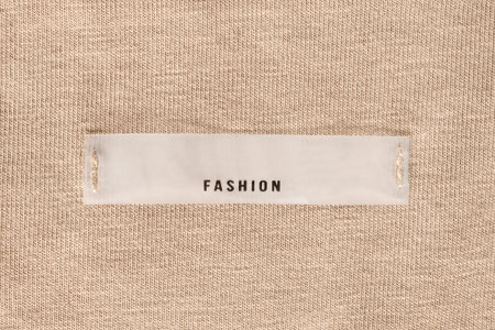 Clothes label says fashion sewn on beige knit fabric background