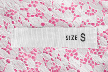 Size S clothes label on white and pink lace background closeup