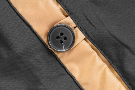 Black clothes button sewn on black and golden fabric closeup