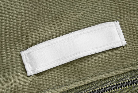 Blank white clothes label stitched on khaki green fabric background closeup