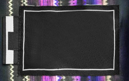 Blank fabric clothes label patch stitched on colorful fabric background closeupの写真素材