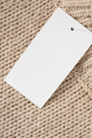 Blank white paper clothes label on beige wool knit background