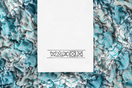 Washing instructions clothes label on light blue wool crumpled fabric closeup
