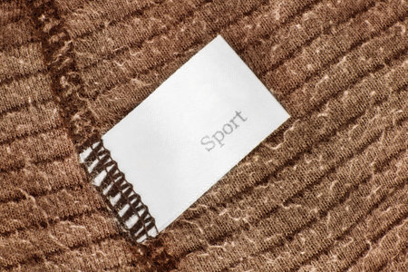 Clothes label says sport on brown knit fabric background closeup