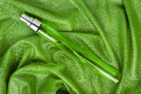 Glass perfume vial lying on green holographic draped fabric backgroundの写真素材