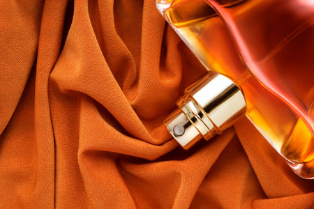 Part of glass perfume bottle closeup lying on orange draped fabric background