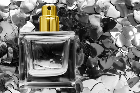 Transparent glass perfume bottle on silver metallic heart confetti backgroundの写真素材