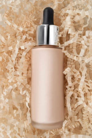 Light beige foundation drops frosted glass bottle lying in crinkle shredded filling paperの写真素材