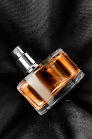 Perfume spray bottle lying on black silk fabric background