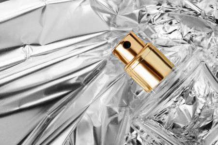 Transparent glass perfume spray bottle lying closeup on crumpled silver foil background