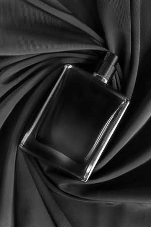 Black glass perfume spray bottle lying on black draped fabric backgroundの写真素材