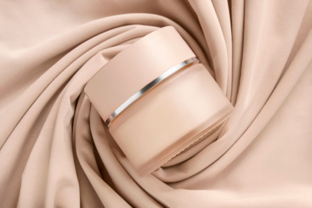 Blank beige cosmetic cream jar lying on draped beige fabric backgroundの写真素材