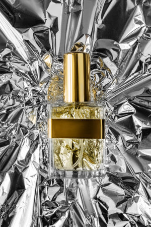 Yellow perfume glass bottle lying on silver crumpled foil backgroundの写真素材