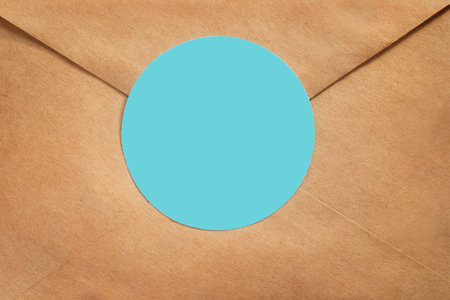 Brown craft paper sealed envelope with blue blank label closeup as a backgroundの写真素材