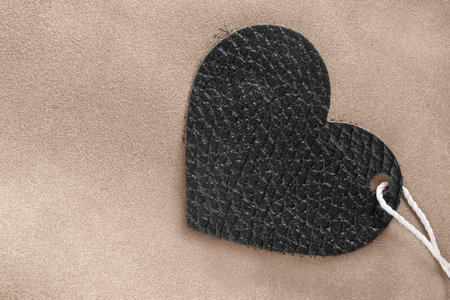 Black leather heart against beige suede background closeupの写真素材
