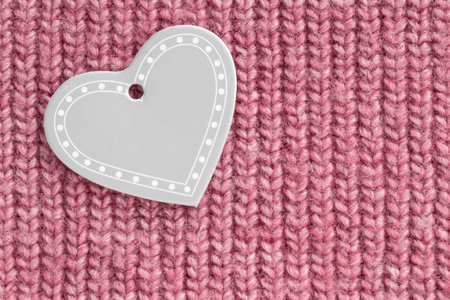 Blank heart shaped label against pink knit wool fabric background closeup