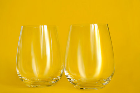 Two empty water glasses standing on yellow studio backgroundの写真素材