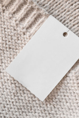 Blank price tag clothes label on beige knit wool fabric background closeup
