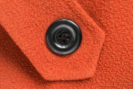 Black clothes button sewn on orange color wool backgroundの写真素材