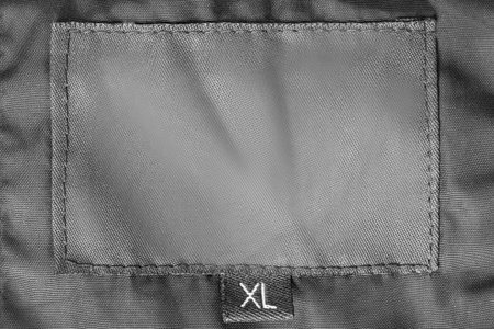 Size XL clothes patch label stitched on black fabric closeup as a background