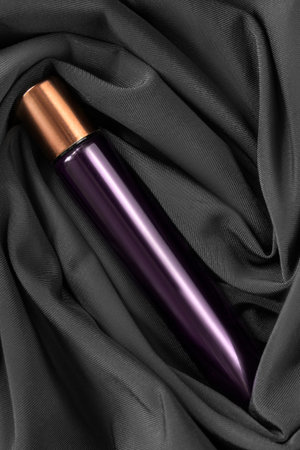 Purple glass perfume vial lying in black draped silk fabric as a backgroundの写真素材
