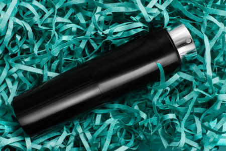 Elegant black perfume travel atomizer case lying in blue shredded packaging paperの写真素材