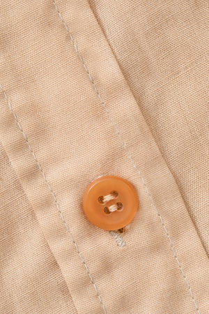 Brown shirt button sewn on beige cotton fabric background closeupの写真素材