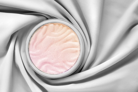 Pink and golden highlighter powder jar wrapped with white draped silk fabricの写真素材