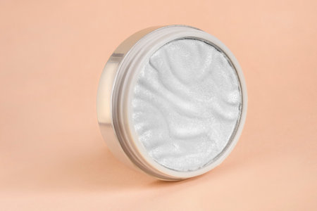 Silver highlighter powder jar over pastel beige studio backgroundの写真素材