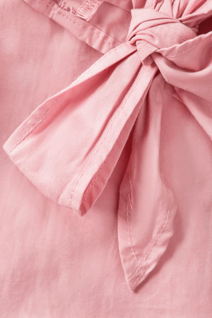 Tied bow detail of pastel pink cotton fabric garment closeup as a backgroundの写真素材