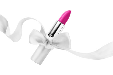 Magenta pink lipstick silver tube tied with white silk ribbon bow isolated over whiteの写真素材