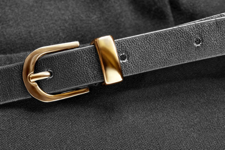 Black leather belt with golden clasp closeup on black fabric backgroundの写真素材