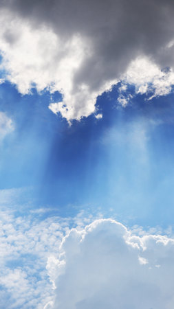 Fluffy clouds highlighted by the sun high in blue skyの写真素材