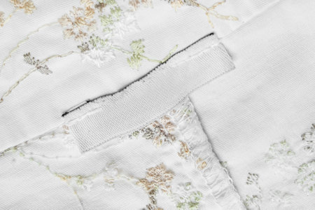 Blank white clothes patch label stitched on embroidered white fabric backgroundの写真素材