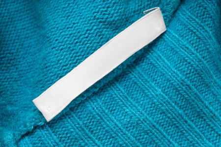 Blank clothes label over blue wool knit fabric background closeup
