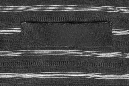 Blank clothes patch label stitched on black and white striped fabric backgroundの写真素材