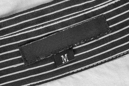 Size M blank clothes label stitched on black and white striped fabric background