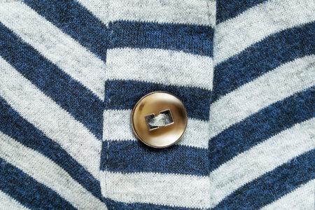 Golden clothes button sewn on striped knit fabric background closeup