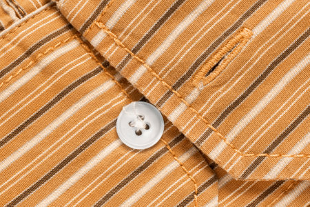 Small shirt button and buttonhole on yellow striped fabric backgroundの写真素材