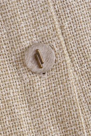 Beige clothes button sewn on beige canvas fabric closeup as a background
