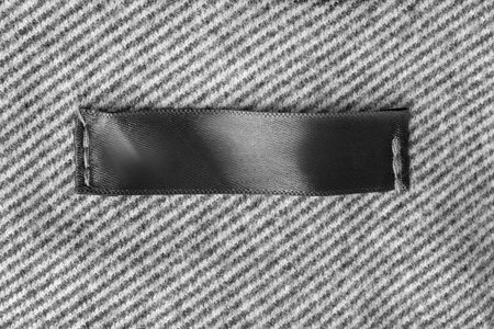 Blank black clothes label stitched on white and black wool fabric background