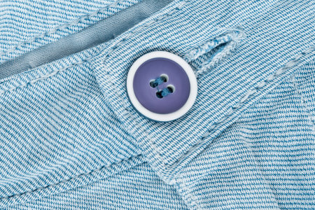Plastic purple pants button closeup on light blue cotton fabric as a backgroundの写真素材